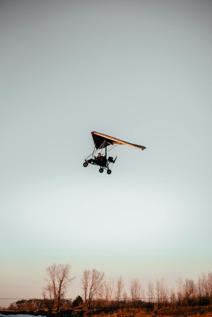 A hang glider flies above the trees during a beautiful sunset.