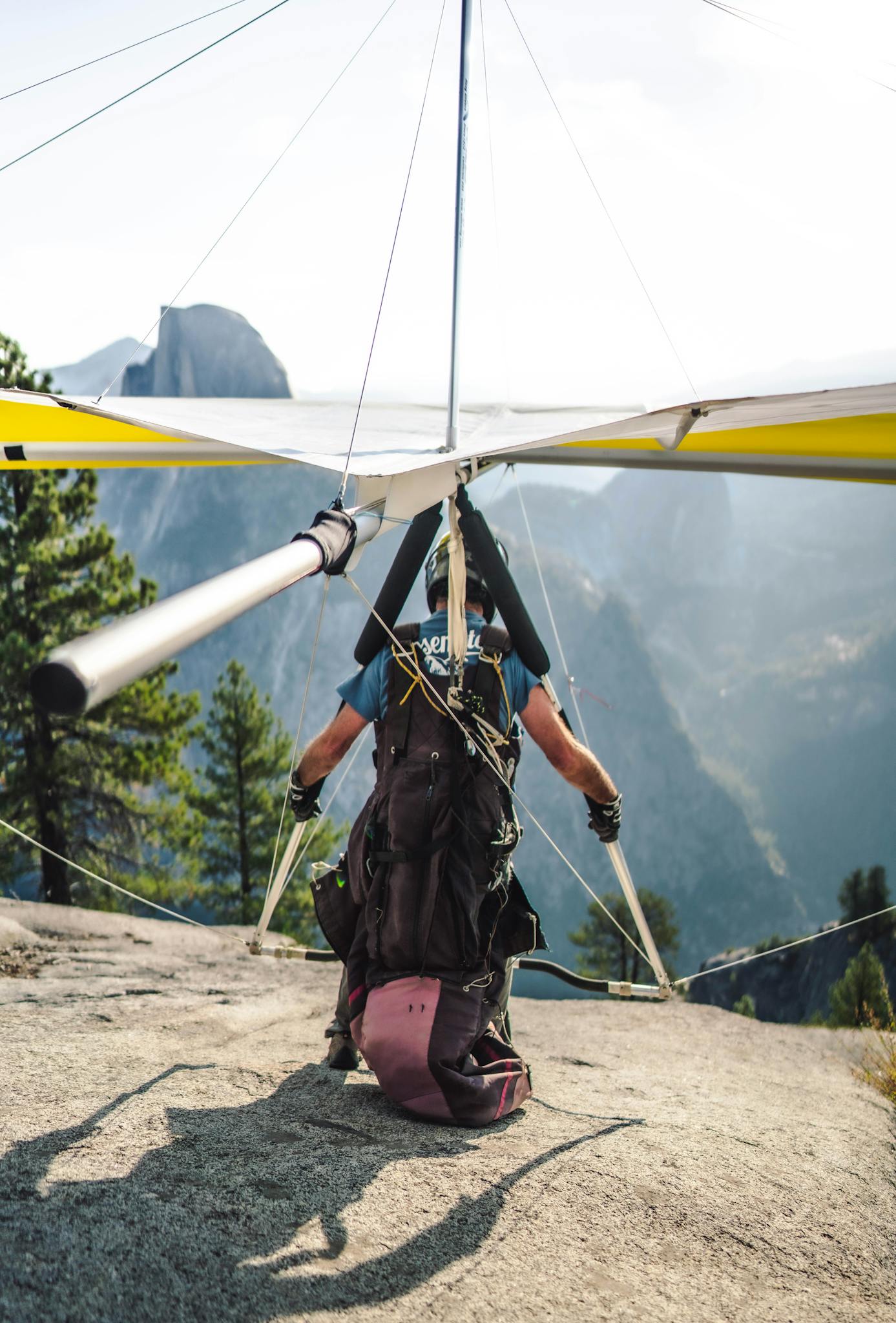 A hang glider prepares to launch from a mountain ledge with a striking view of distant peaks.