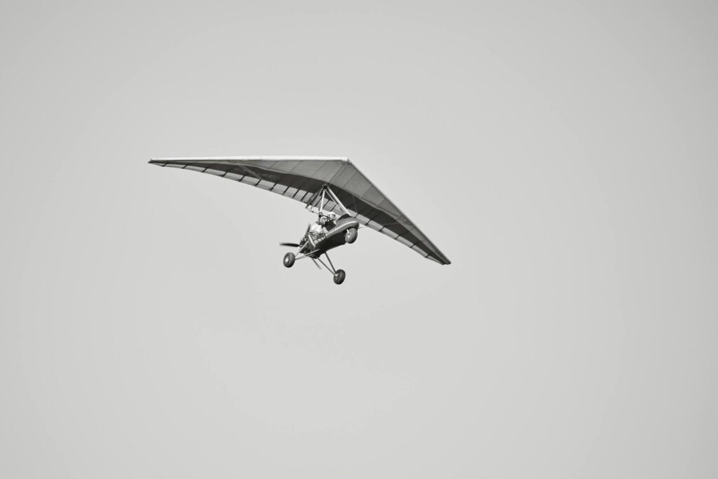 A stunning black and white photo of a motorized nanolight trike flying freely in a clear sky.