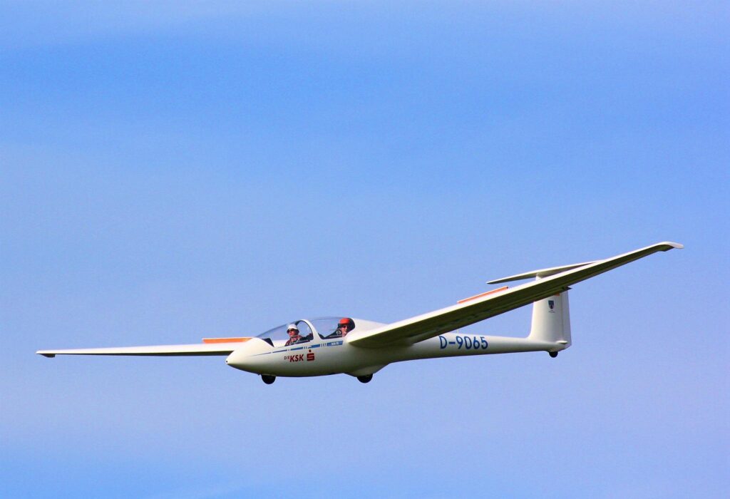A two-seater glider flying gracefully against a backdrop of clear blue sky.