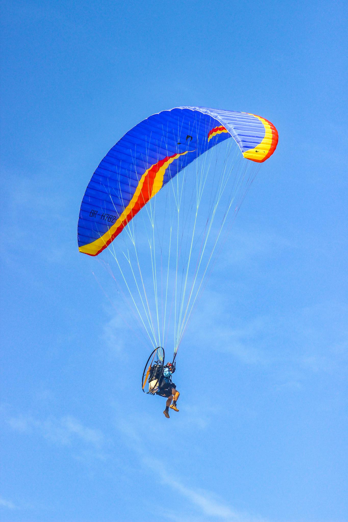 Experience the thrill of paragliding with this breathtaking image of a lone paraglider in flight against a brilliant blue sky.