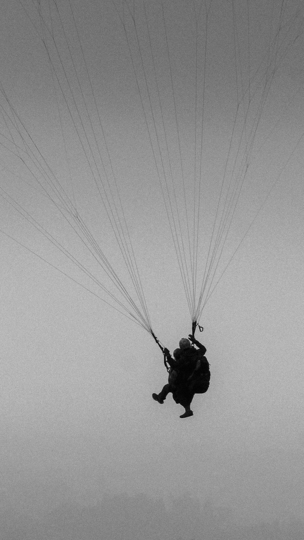 Silhouetted tandem paragliding against a misty, overcast sky creates a dramatic monochrome scene.